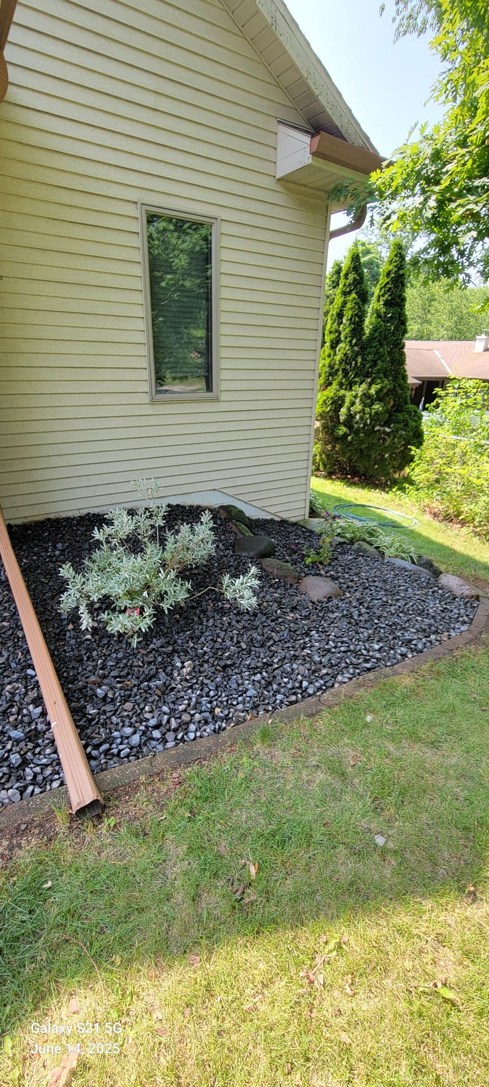 Modern landscaping with black gravel, shrubs, and a light-colored house exterior.