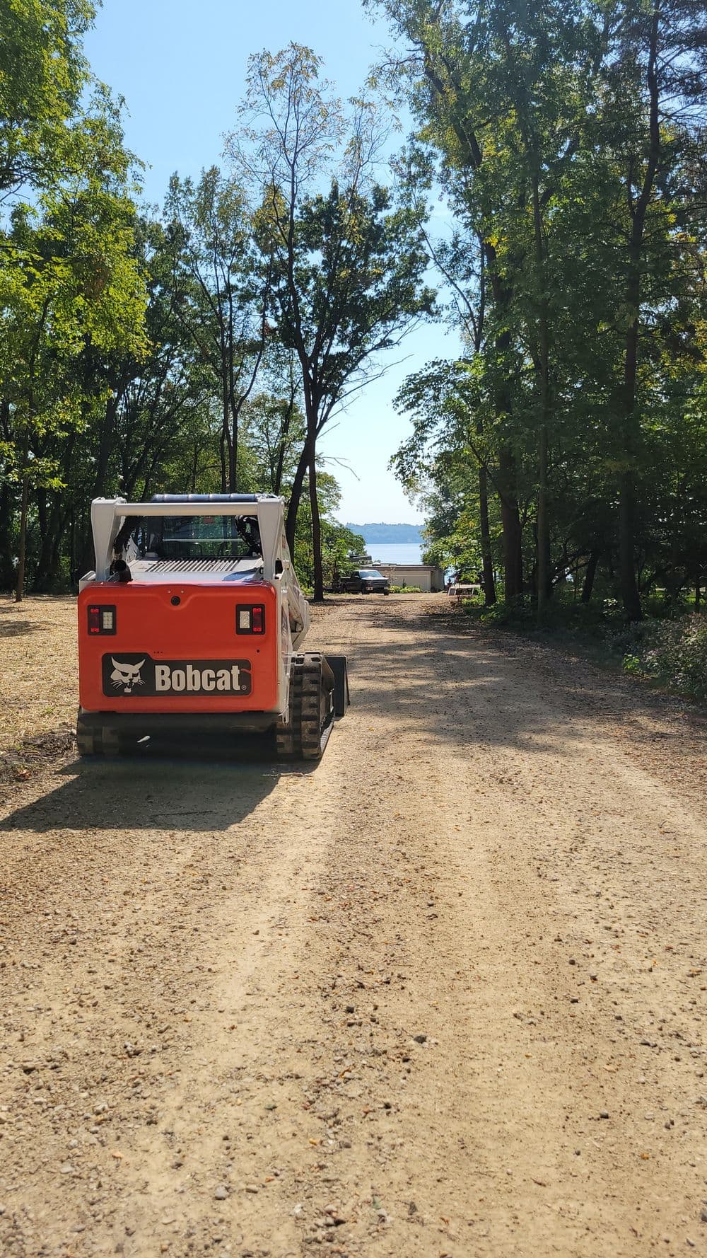 Bobcat skid steer on a dirt road leading to a serene waterfront view.