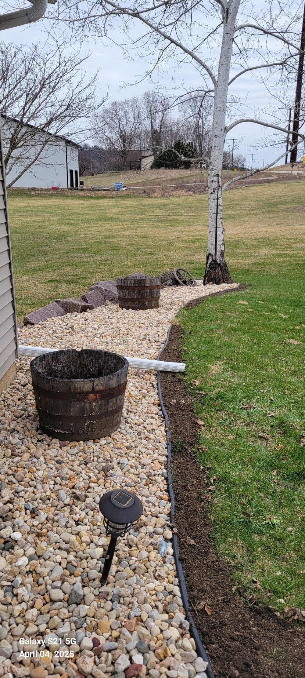 Flowerbed featuring stone landscaping, wooden planters, and solar lights beside a tree.