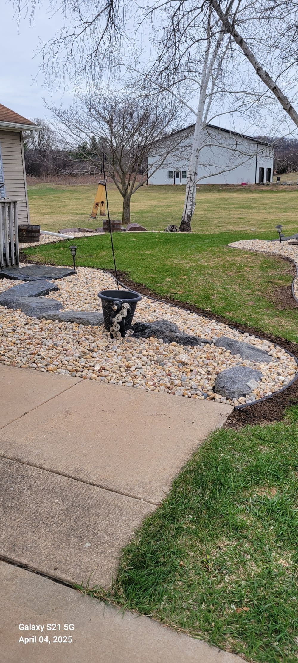 Garden landscape with decorative stones, planter, and green lawn on a sunny day.