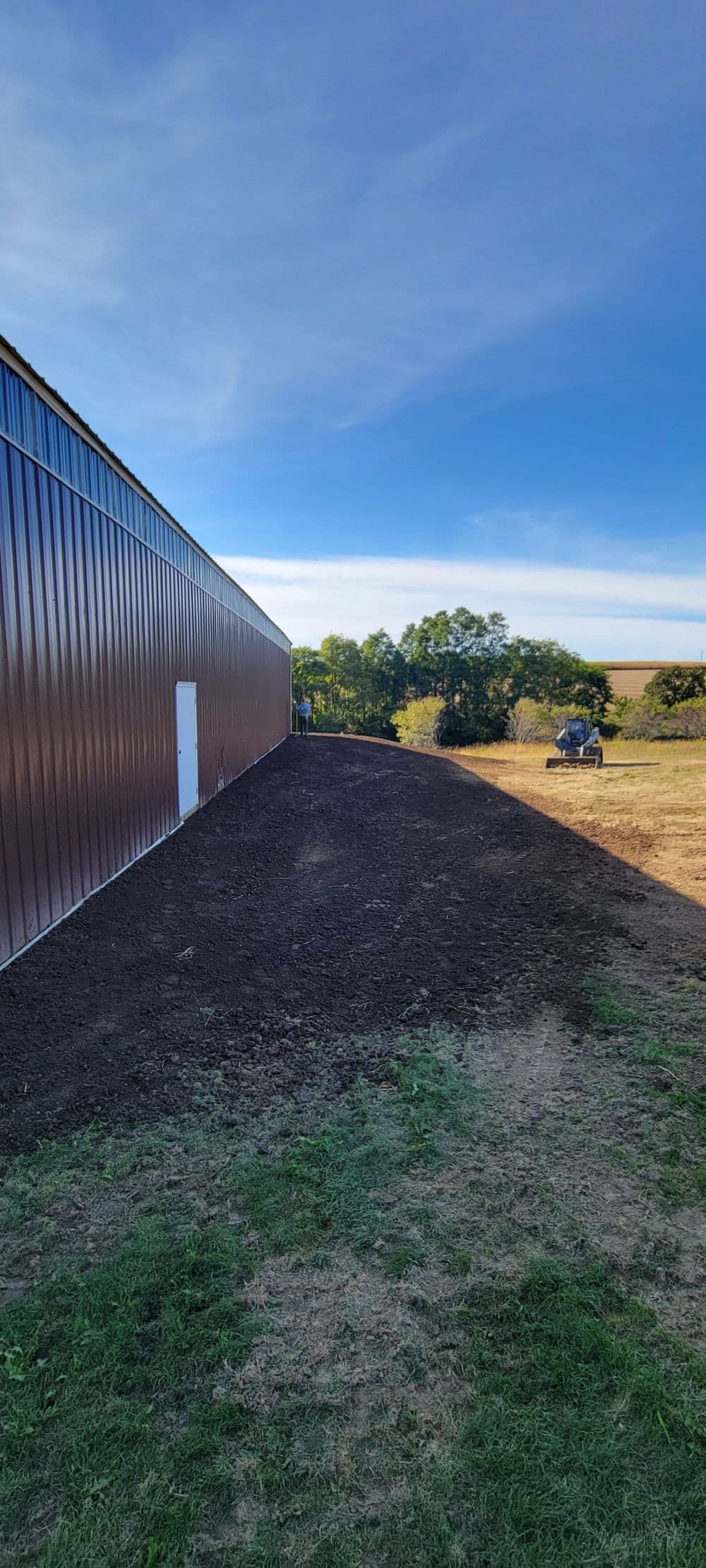 Open field beside a barn, freshly tilled soil under a clear blue sky.