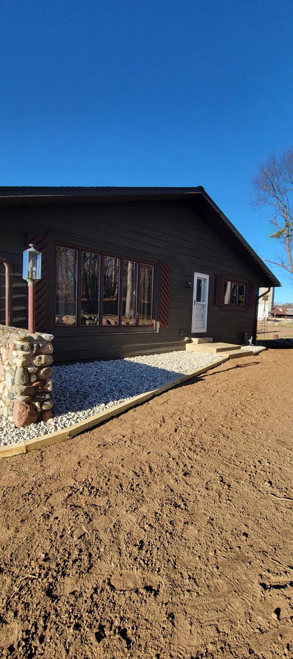 Modern brown house with large windows and stone accents, set against a clear blue sky.